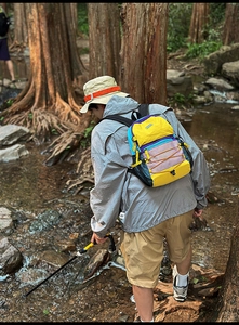 Outdoor hiker wearing a colorful patchwork backpack by a forest stream for hiking