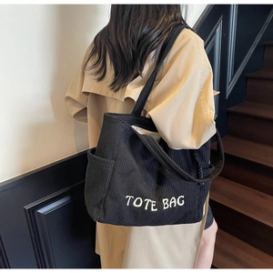 Vue détaillée du sac cabas en velours côtelé noir avec broderie blanche et poche latérale