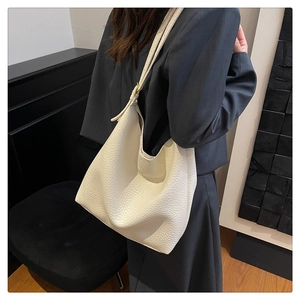 Close-up of minimalist large white pebble grain bucket bag worn on shoulder by a model