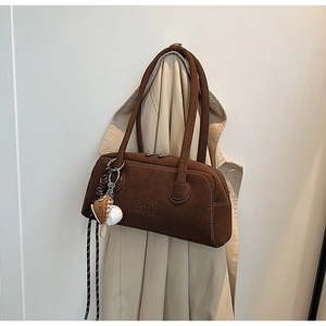 Close-up of brown suede Boston bag with embossed lettering and baseball glove charm