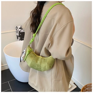 Detail view of avocado green suede croissant bag with cow print charm and rope strap