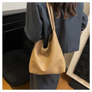 Detailed view of a tan pebble leather tote bag worn by a model in a modern interior
