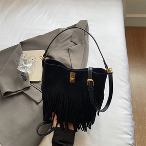 Detail of black fringe bucket bag with vintage gold twist lock on white bedding