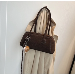 Detail of dark brown suede shoulder bag with contrast stitching and baseball charm