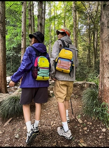 Outdoor backpacks in color-block design worn by hikers on a forest trail path