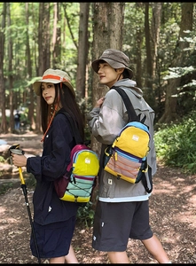 Outdoor color-block backpack and bucket hat displayed in a scenic forest environment