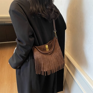 Detail of a dark brown suede shoulder bag featuring long fringe tassels and golden metal buckle