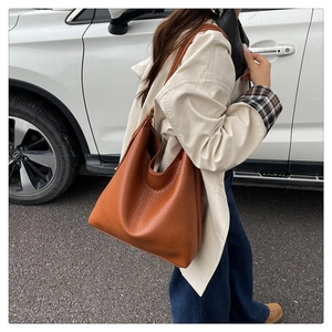 Brown grainy leather hobo bucket bag shown on a model's shoulder in an outdoor street setting