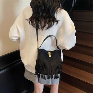 Detail of black suede bucket bag featuring fringe trim and golden rotating metal lock