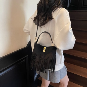 Close-up of black fringe shoulder bag with golden clasp on a model in a natural setting