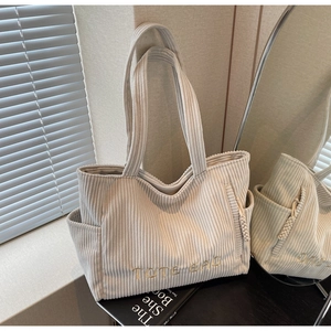 Détail du sac cabas en velours côtelé beige avec broderie posé sur un livre