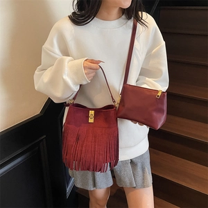 Detail of red tassel bucket bag set showing matte suede texture and gold metal buckle
