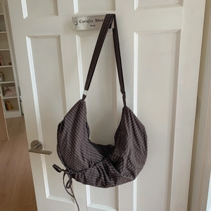 Detail view of brown checkered hobo bag with drawstring base on white wooden door