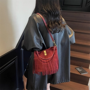 Detail of burgundy fringe crossbody bag with gold twist lock on suede leather texture
