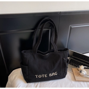 Détail du sac cabas en velours côtelé noir avec broderie TOTE BAG sur un bureau