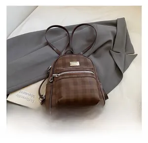Détail d'un mini sac à dos à carreaux marron foncé sur un blazer gris avec zip argent