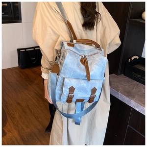 Detail showing blue denim canvas texture and brown leather strap accents on the backpack