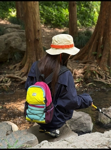 Detail of color-block hiking backpack with a bucket hat and trekking pole in nature
