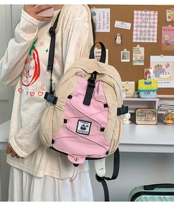 Detail of a beige and pink nylon backpack featuring an adjustable strap and cute patch