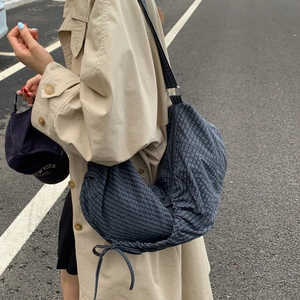 Outdoor view of a navy plaid canvas crossbody dumpling bag worn with a beige trench coat