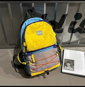 Detail of color-block nylon backpack featuring white mesh pocket and orange bungee cord decoration