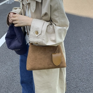 Outdoor shot of a brown suede bucket bag with a small matching pouch charm on the side