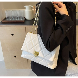 Chic white quilted crossbody bag with gold chain strap shown on a model in soft light