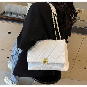 Detail of white quilted crossbody bag with gold chain strap worn with a black blazer