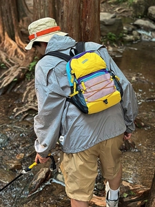 Outdoor color-block hiking backpack shown on model amidst natural forest and stream scenery