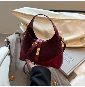 Close-up of a burgundy leopard embossed handbag with gold turn-lock and leather buckle details