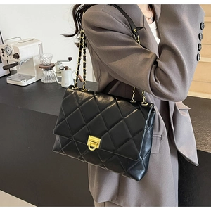 Detail einer schwarzen gesteppten Umhängetasche mit goldener Kette auf grauem Blazer