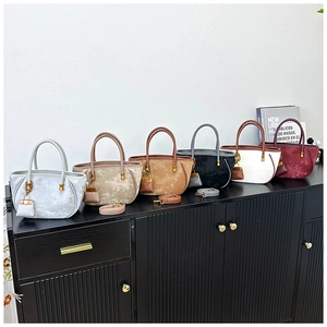 Six colors of suede bucket bags with gold hardware and mini bag charms on a wooden shelf