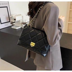 Detail einer schwarzen Stepptasche mit Goldkette, getragen als Schultertasche