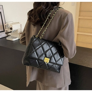 Model wearing a black quilted leather chain bag with gold hardware and flap closure
