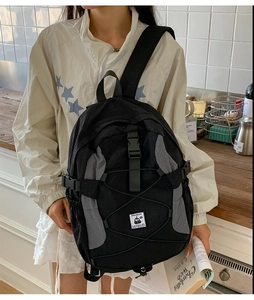 Detail of black backpack showing grey honeycomb texture, elastic bungee cords and penguin patch