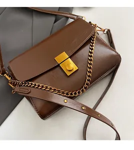 Détail du sac à bandoulière en cuir brillant marron foncé avec boucle dorée
