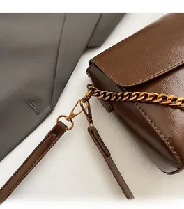 Détail de la bandoulière chaîne dorée avec fermoir mousqueton sur un sac marron