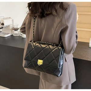 Detail einer schwarzen Stepptasche mit goldener Kette, getragen von einem Modell