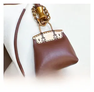 Detail of a brown leather mini bag charm with gold chain on a white bucket bag handle