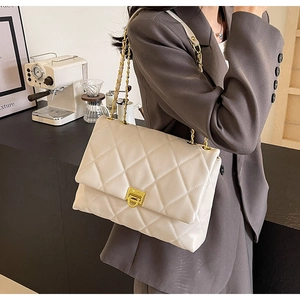 Detail der cremeweißen Stepptasche mit goldenem Drehverschluss und Kettenriemen