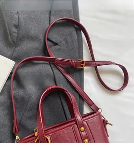 Detailansicht der weinroten Beuteltasche mit goldenen Nieten auf grauem Blazer