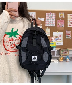 Asian female model holding a gray and black nylon backpack in a cozy office setting
