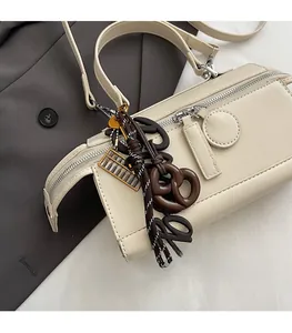 Detail of cream leather crossbody bag with unique pretzel and golden abacus charms