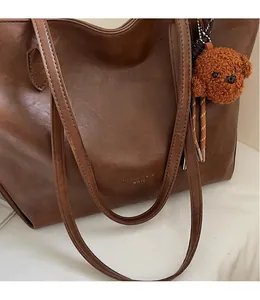 Detail of smooth shoulder strap and cute bear charm on brown faux leather tote bag