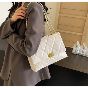 Detailed view of white quilted chain bag with gold metal clasp on model's shoulder