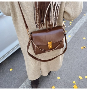 Détail du sac bandoulière en cuir marron avec boucle dorée sur un décor d'automne