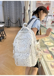 White backpack with star print and plush pendant shown on model in cafe setting