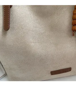 Close-up of beige suede tote bag texture with leather handle and wooden bead charm