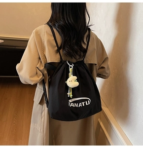 Detailansicht der Rückseite eines schwarzen Nylon-Rucksacks mit Logo und Plüsch-Anhänger