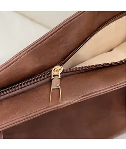 Macro view of brown leather tote showing the gold zipper and inner fabric lining detail